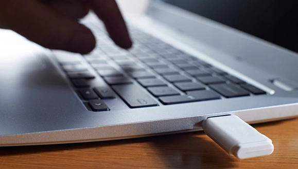 A close-up of a person about type on a laptop inserted with a white USB stick.