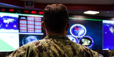 A US Navy Sailor stands and watches a demonstration in a command center.