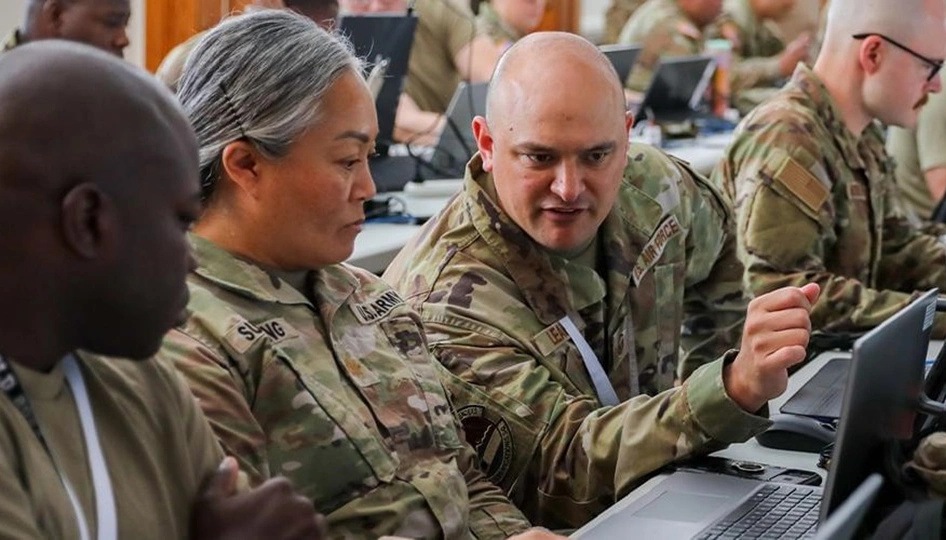 U.S. military personnel consult in front of a laptop.