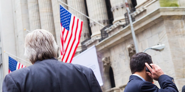 Two men in suits outside a government building with American flags.