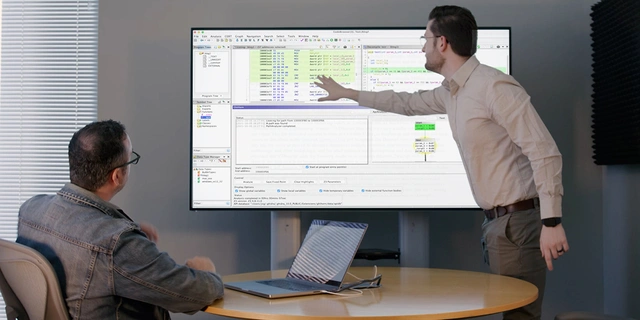 Two colleagues reviewing code on a large screen.