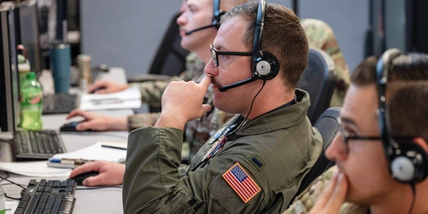 US Airmen wearing headsets while working at computers.