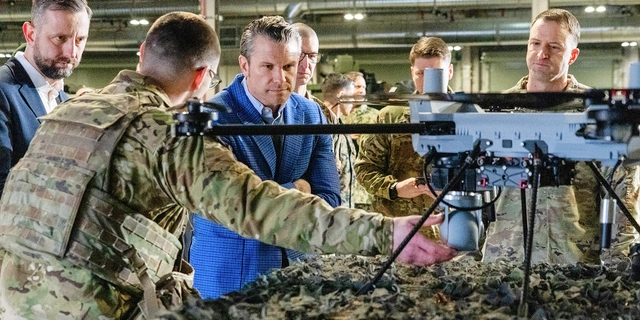Secretary of War Pete Hegseth and military personnel examine a drone indoors.