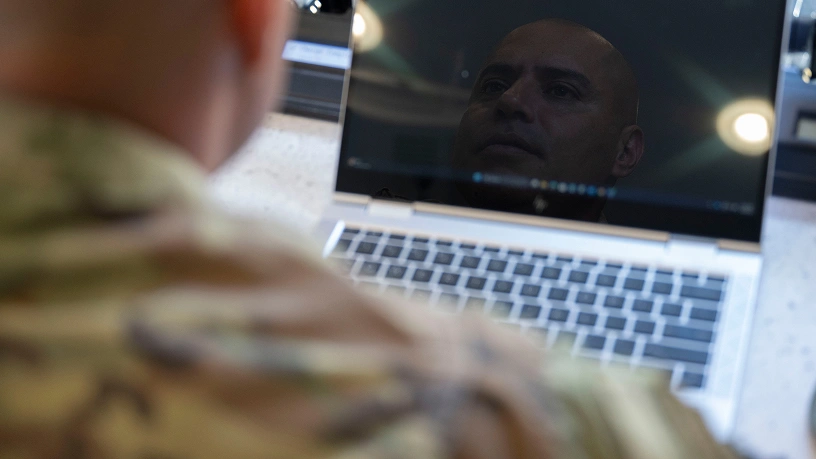 Close-up of a service member using a laptop, with their face reflected on the screen displaying a software interface.