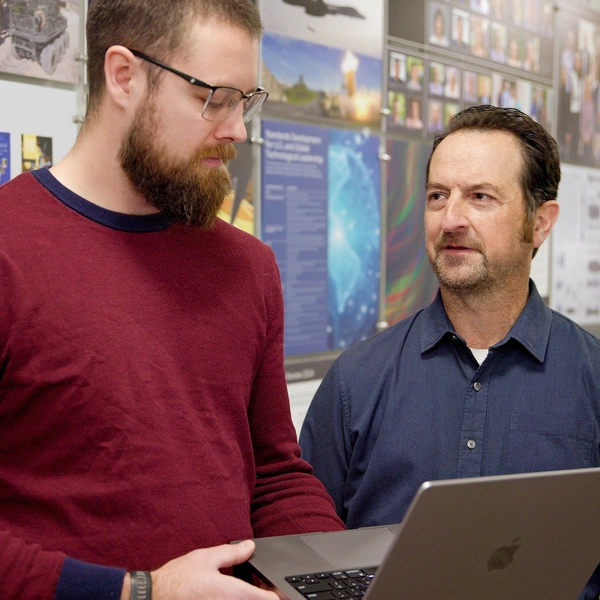 Two SEI employees use a laptop to review a project together in the office.