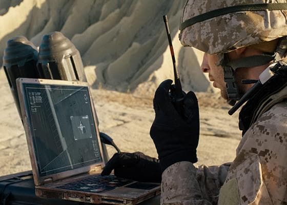 Soldier using walkie talkie and laptop computer in a desert